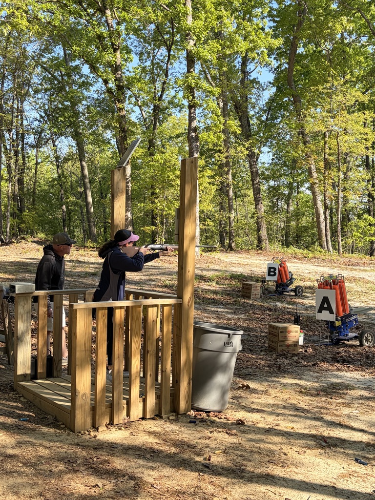 Shooter aiming from a wooden sporting clays stand with throwers marked A and B