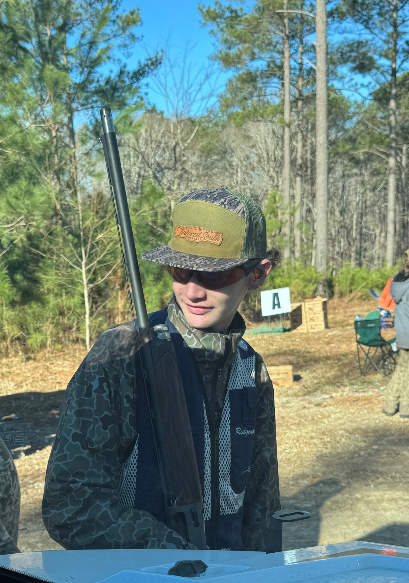 Shooter in camo and a team vest carrying a shotgun near the Station A sign