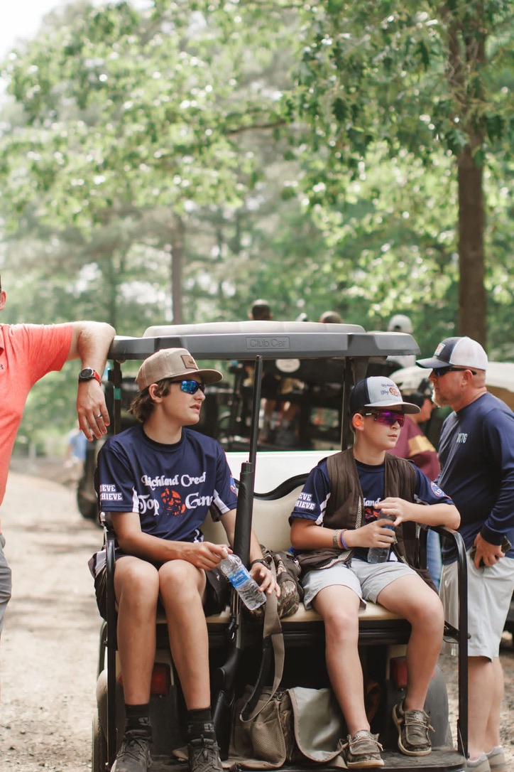 Two Top Guns shooters resting on a golf cart between rounds