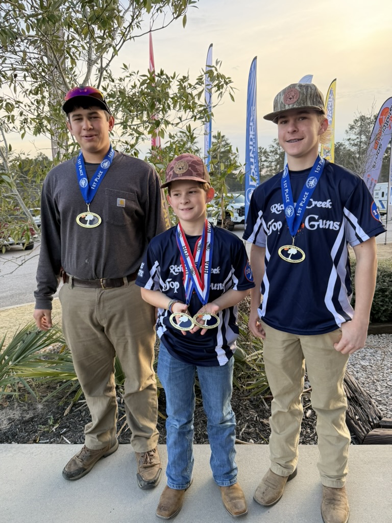 Three Top Guns shooters wearing first place medals at sunset