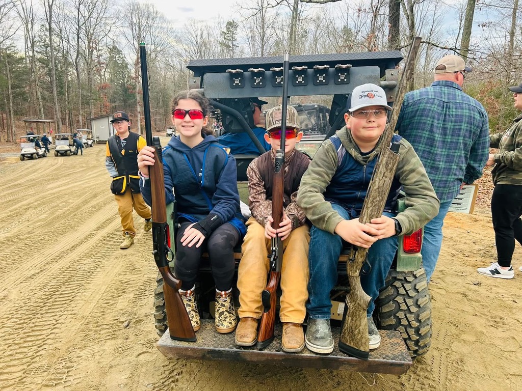 Three young shooters with shotguns seated on the back of a utility vehicle