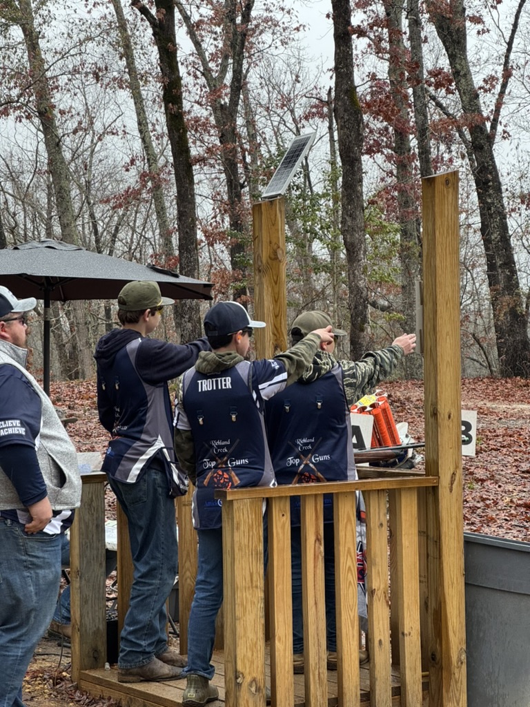 Coach pointing out the target line to shooters at a sporting clays station