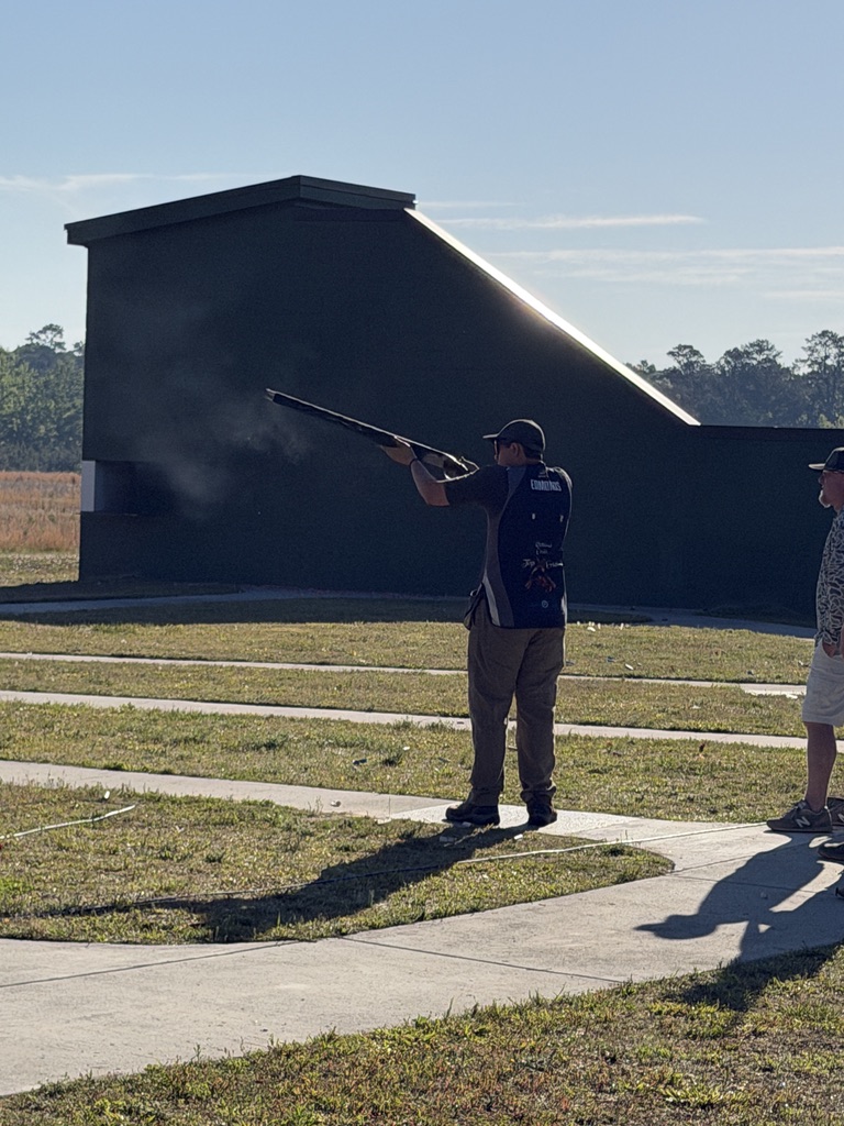 Young shooter firing at a skeet target beside the high house