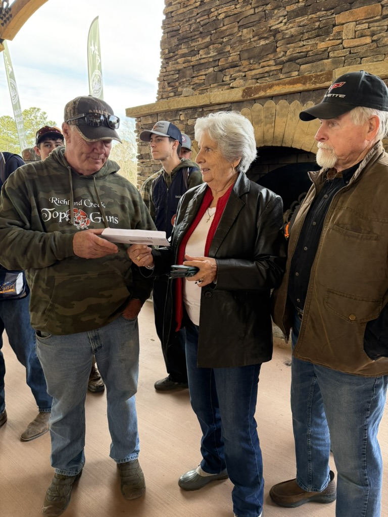 Coach in a Top Guns hoodie reviewing score sheets with parents under a stone pavilion