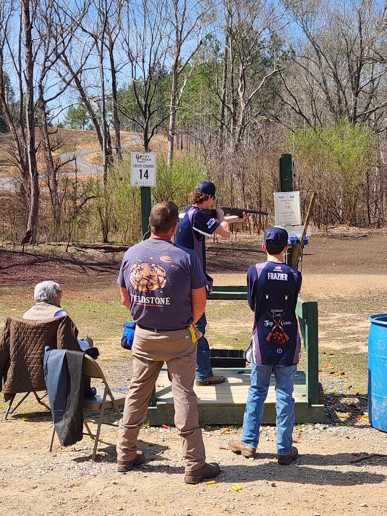 Shooter firing at station fourteen while teammates and a coach watch