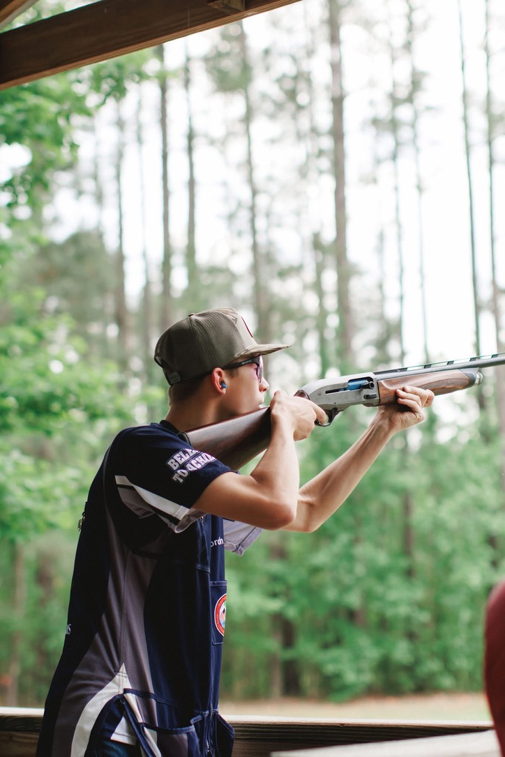 Shooter in a Top Guns jersey mounted on a shotgun inside a covered trap station