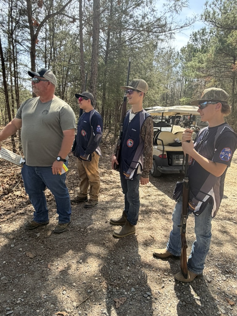 Coach and three shooters waiting beside a golf cart on a wooded sporting clays course