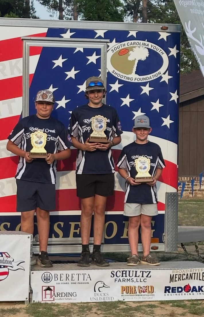 Three Top Guns shooters holding trophies on a podium at the SC Youth Shooting Foundation state shoot