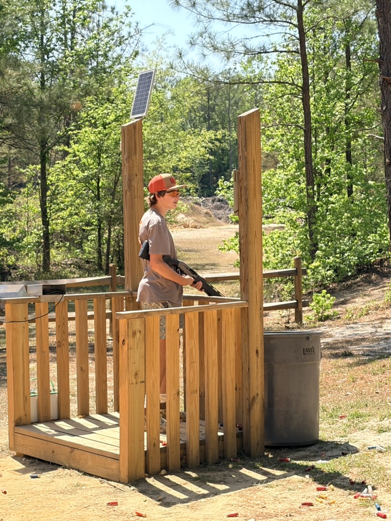Young shooter waiting in a wooden sporting clays station surrounded by trees