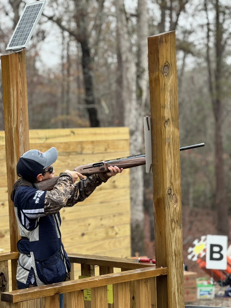 Young shooter aiming a shotgun from a wooden sporting clays station