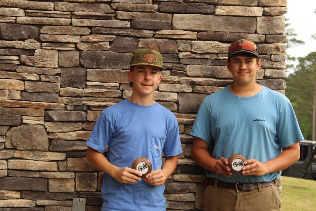 Two Top Guns shooters holding 4-H award plaques against a stone wall