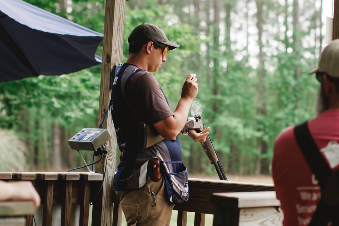 Shooter in a team vest loading a shell into a shotgun at a covered station