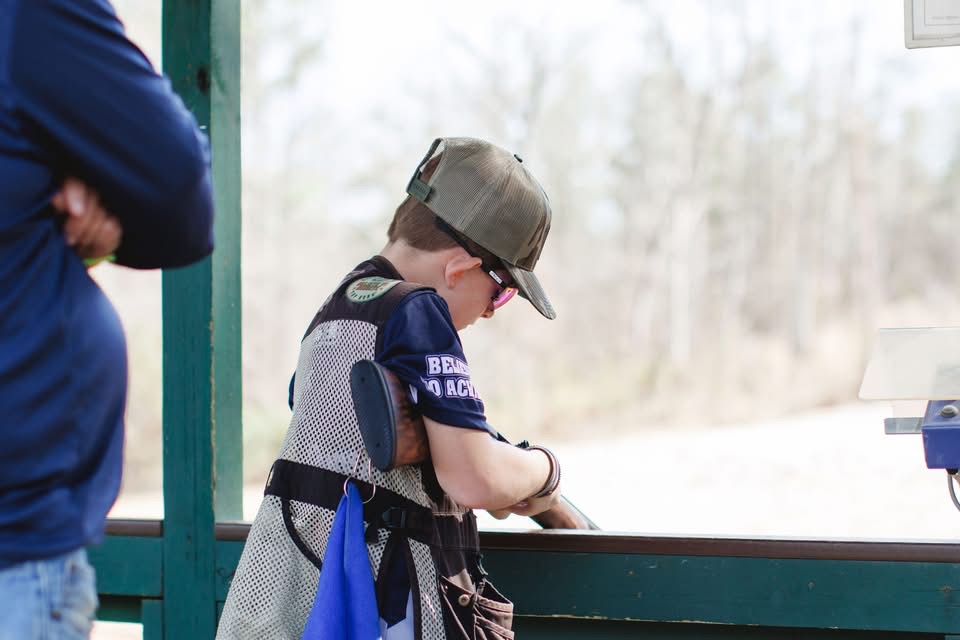 Young shooter loading a shotgun under a covered skeet station