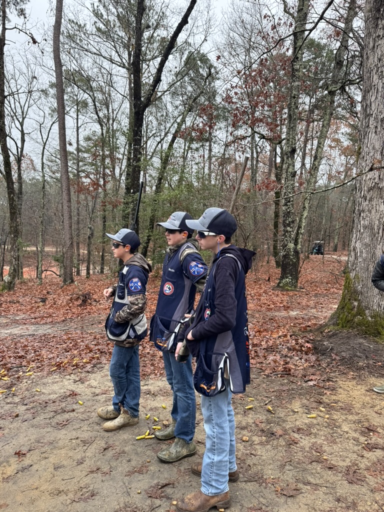 Three Top Guns shooters in vests and caps standing on a leaf-covered course