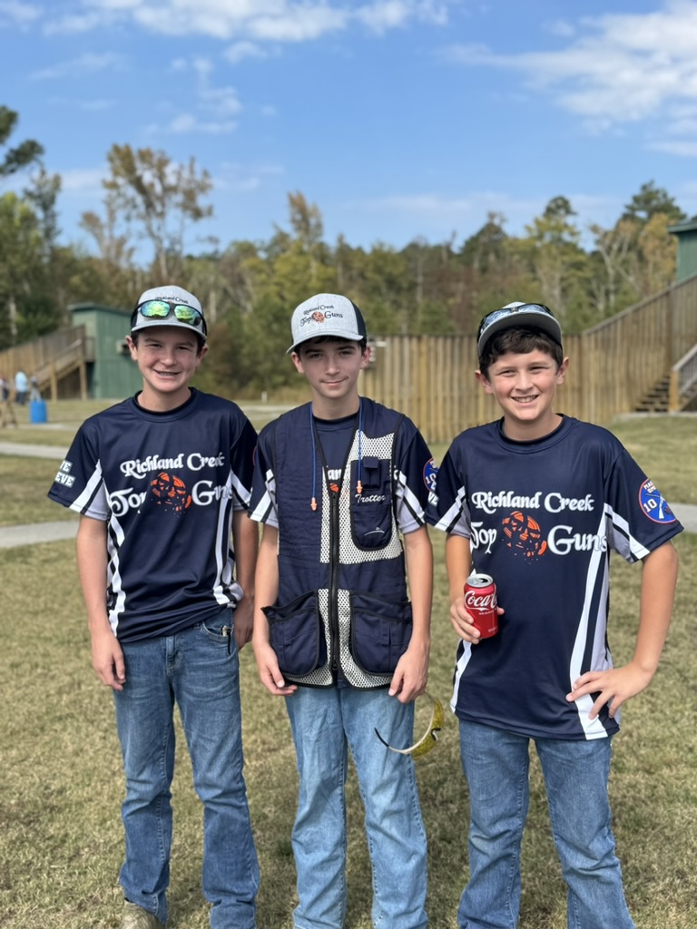 Three Richland Creek Top Guns shooters posing in team jerseys on the grass